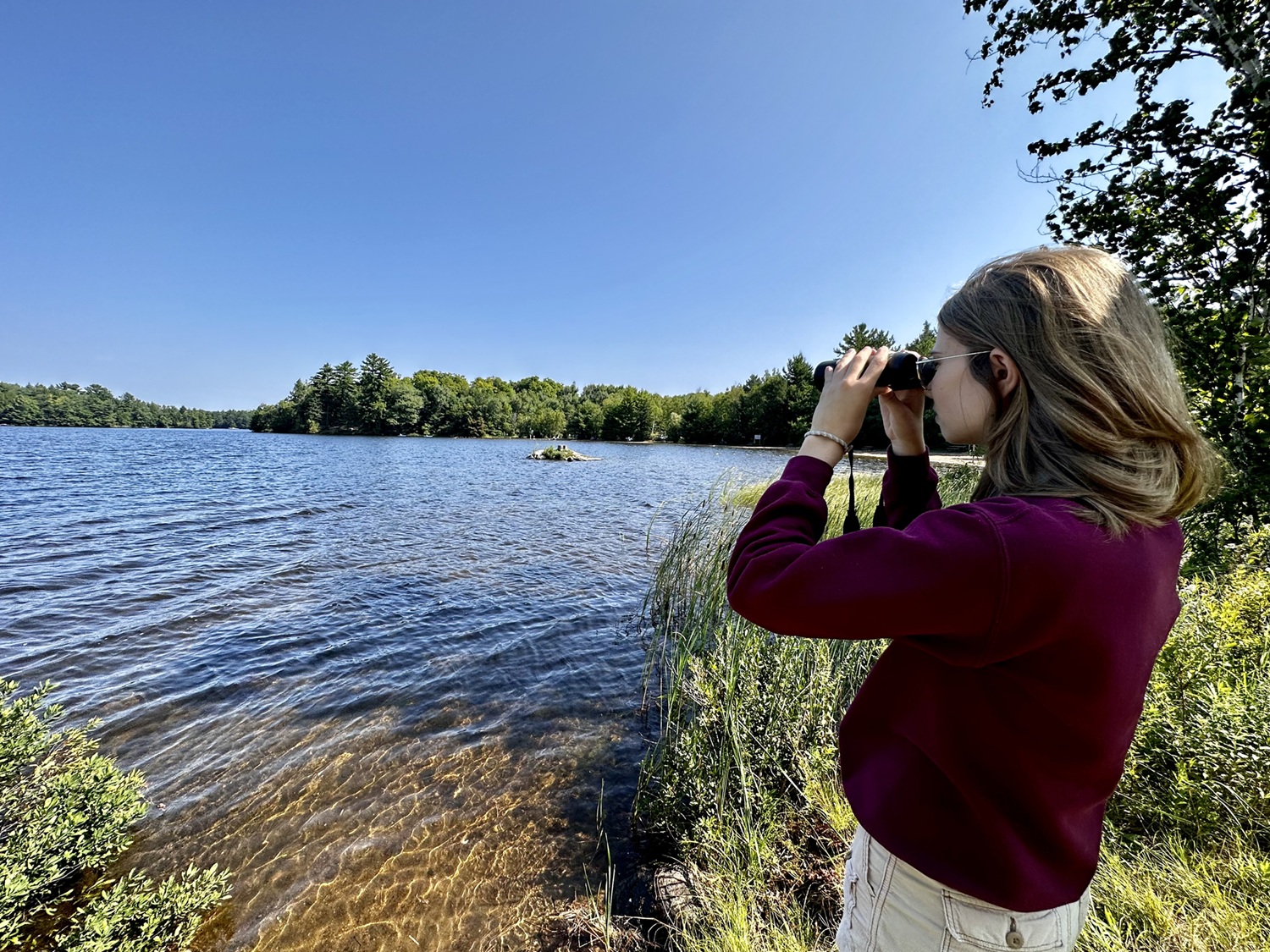 woman looking through binoculars at lake's edge