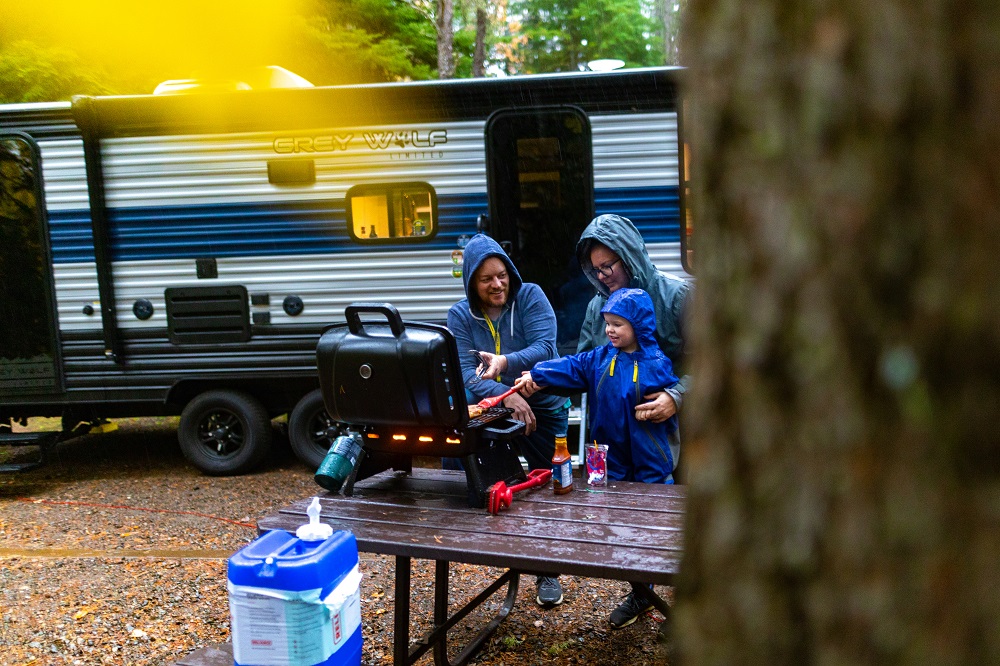 family preparing dinner standing outside of RV on campsite