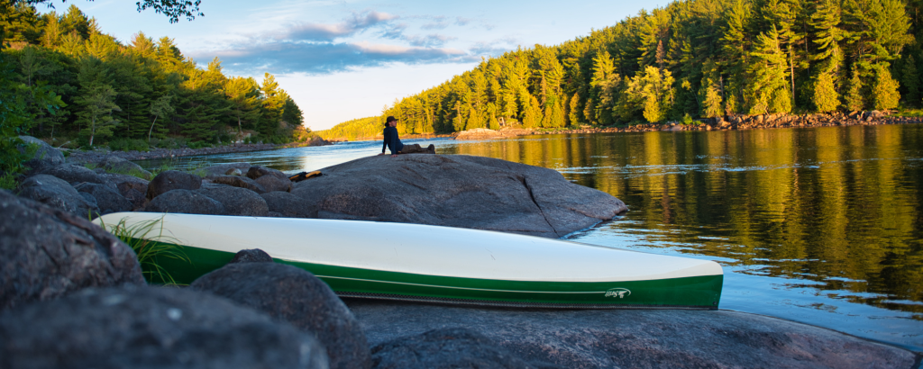 Visitor relaxing on rock behind canoe on river