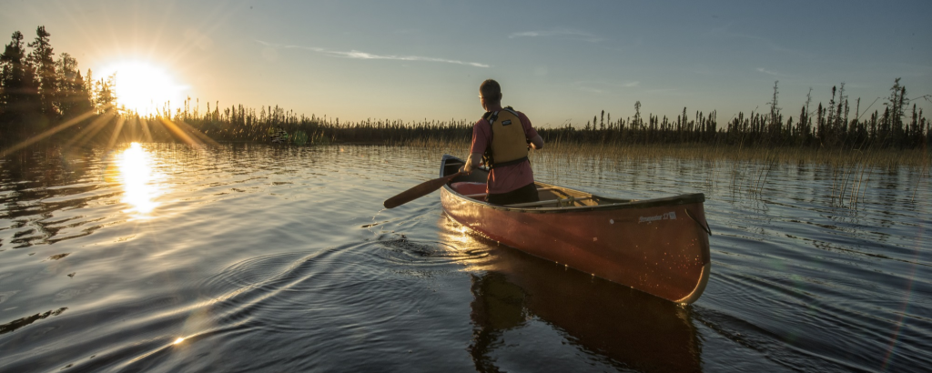 A solo canoeist paddling on a lake towards a sunset
