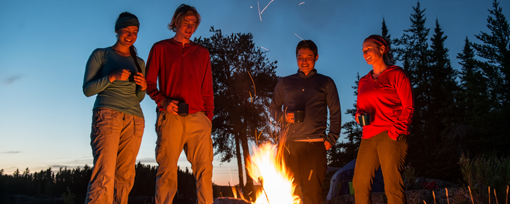 Four people standing around a campfire at night