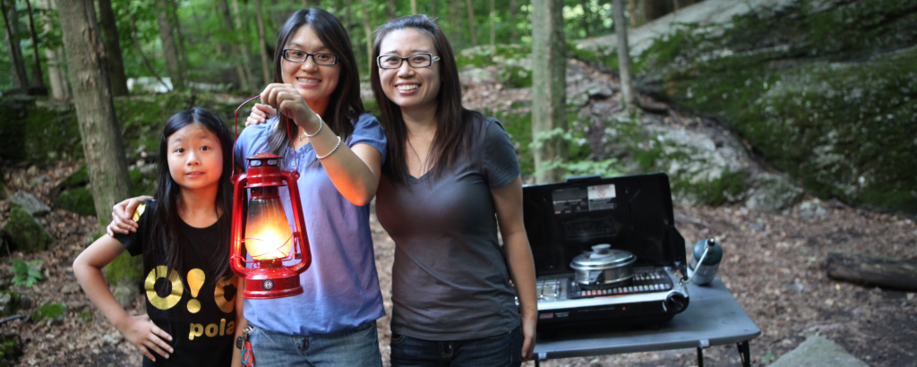 Three people looking at a lantern on their campsite