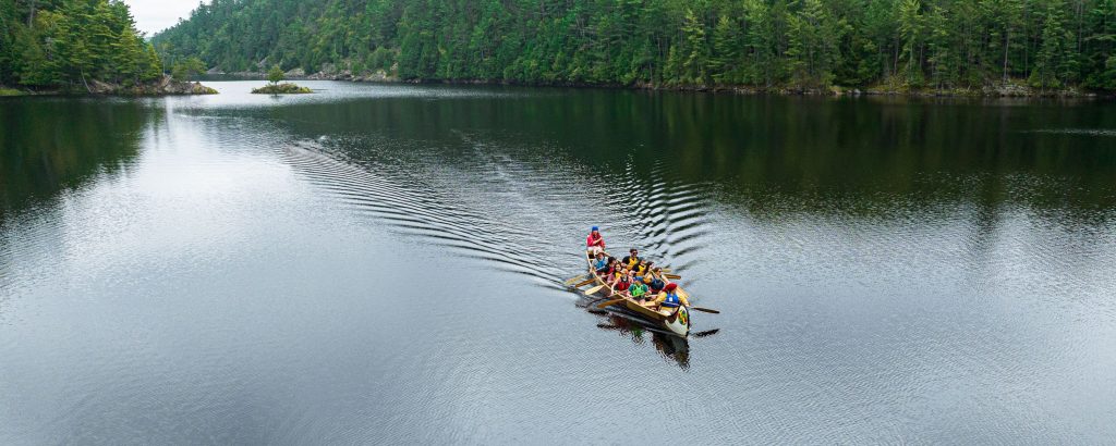Vue aérienne d’un canot de voyageurs rempli de personnes participantes, pagayant sur un lac