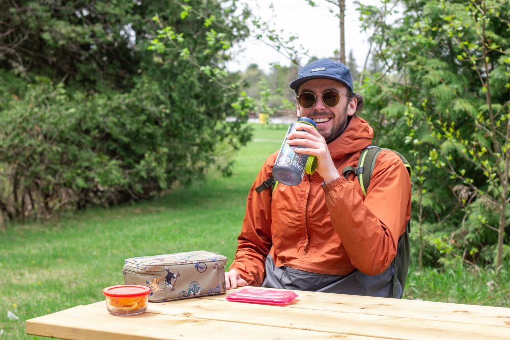 person sitting at picnic table drinking from reusable water bottle