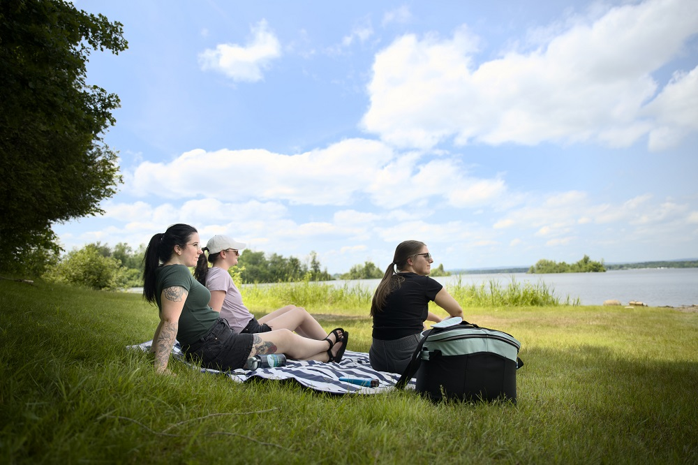 group sitting on beach towel in grass looking out at lake
