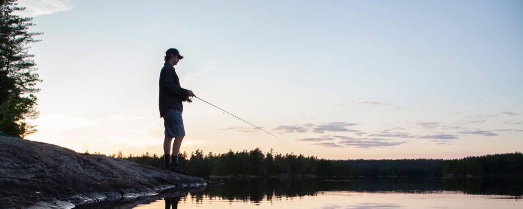 silhouette of person fishing on shoreline at sunset