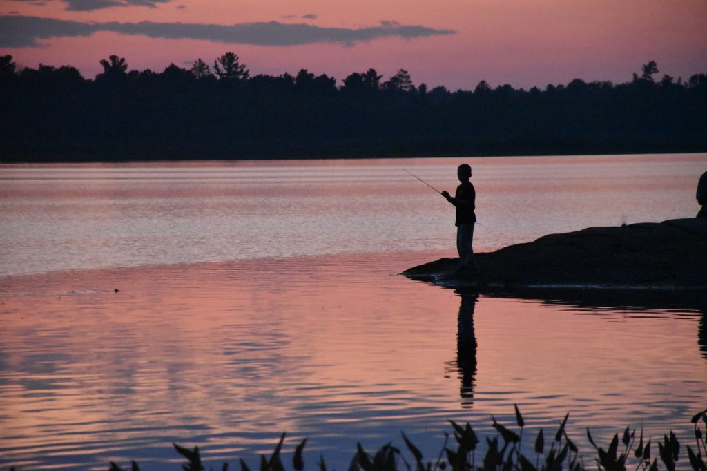 silhouetted fisher on lakeshore