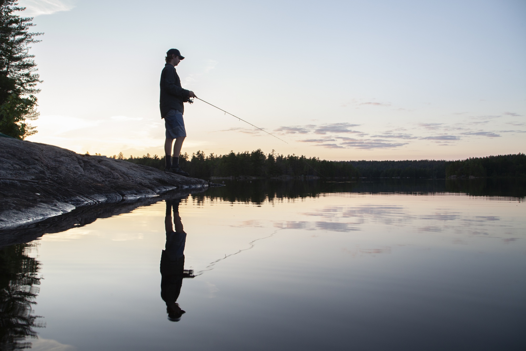 silhouette of person fishing on shoreline at sunset