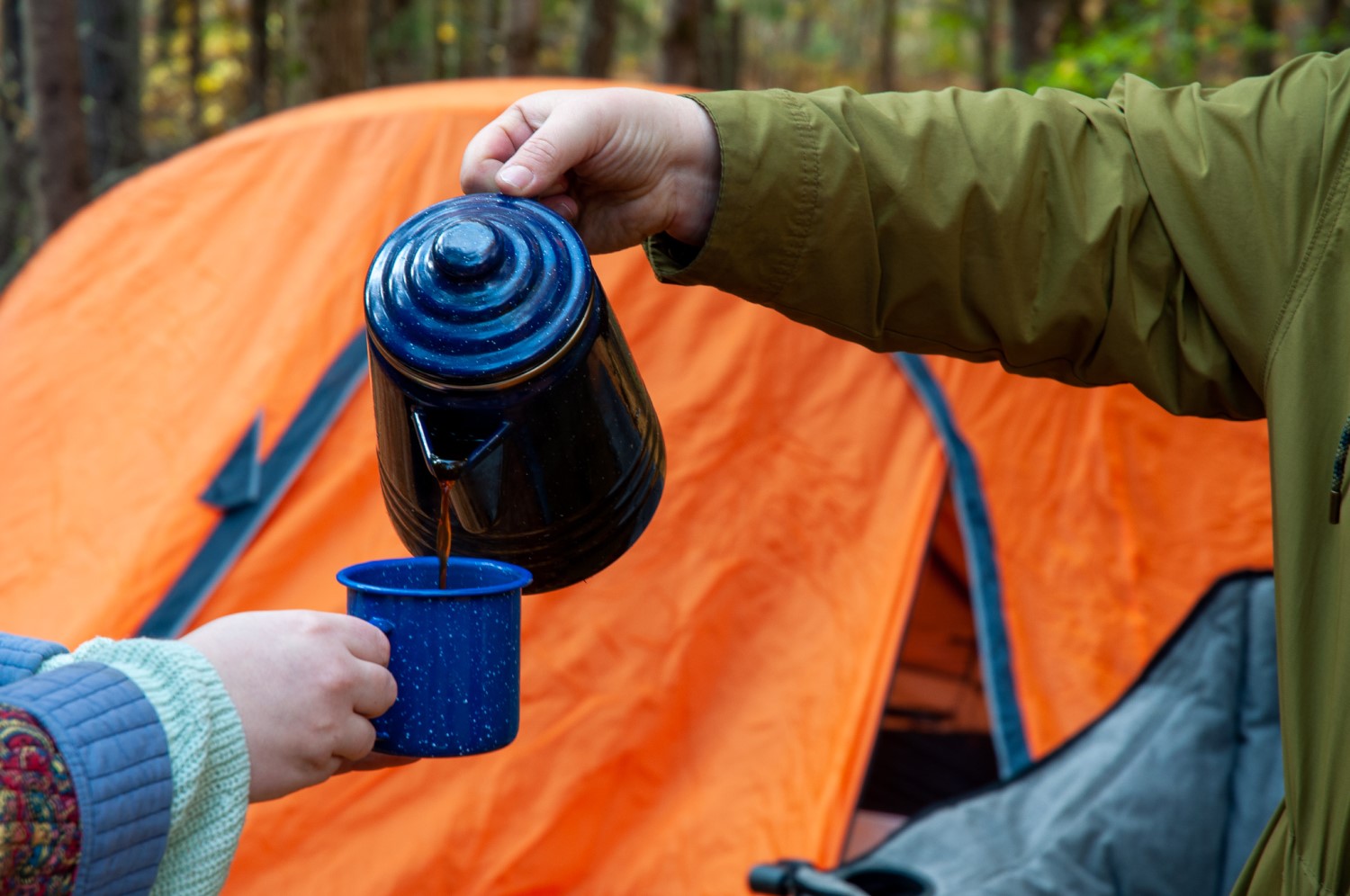 One person's hands holding an enamel coffee pot, pouring into a mug held by another person's hand.