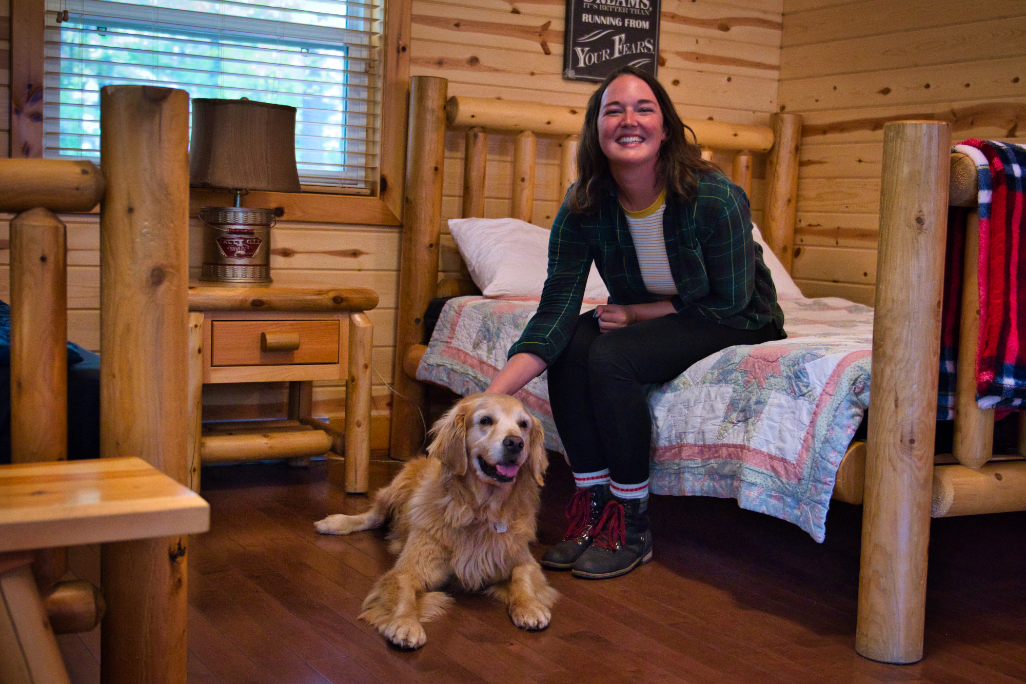 A person sitting on a bed inside a cabin, with their dog on the floor beside them