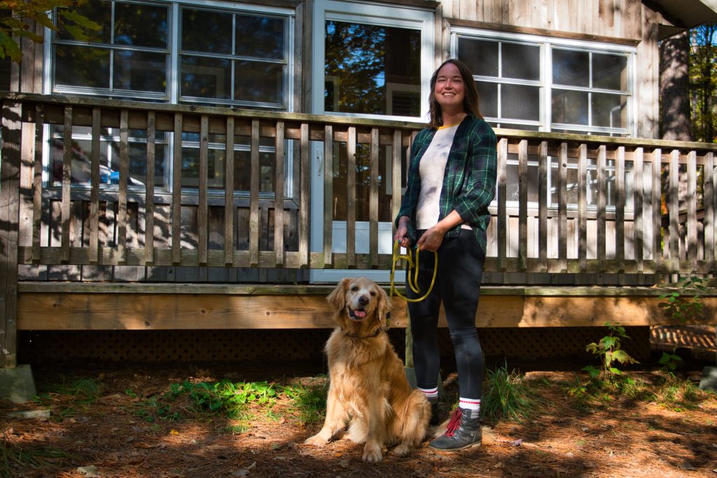 A person with a dog on leash standing outside of a cabin