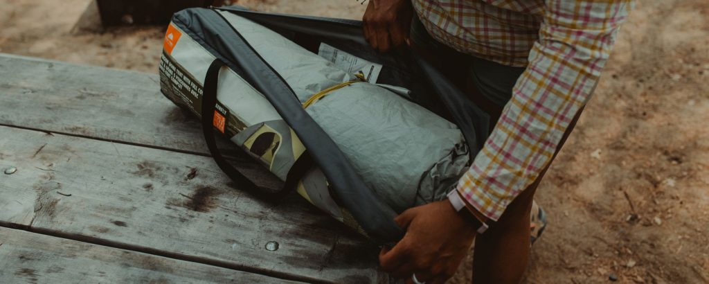person unpacking tent from bag on top of picnic table