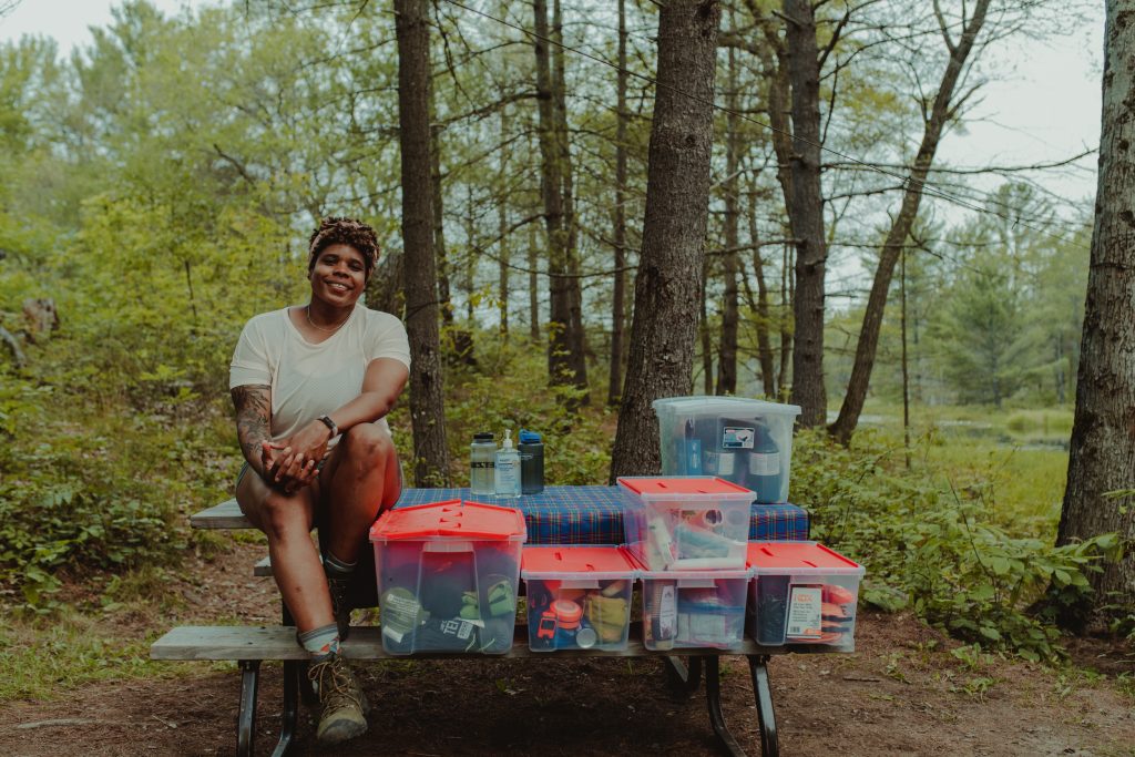 woman sitting beside totes filled with camping equipment on campsite