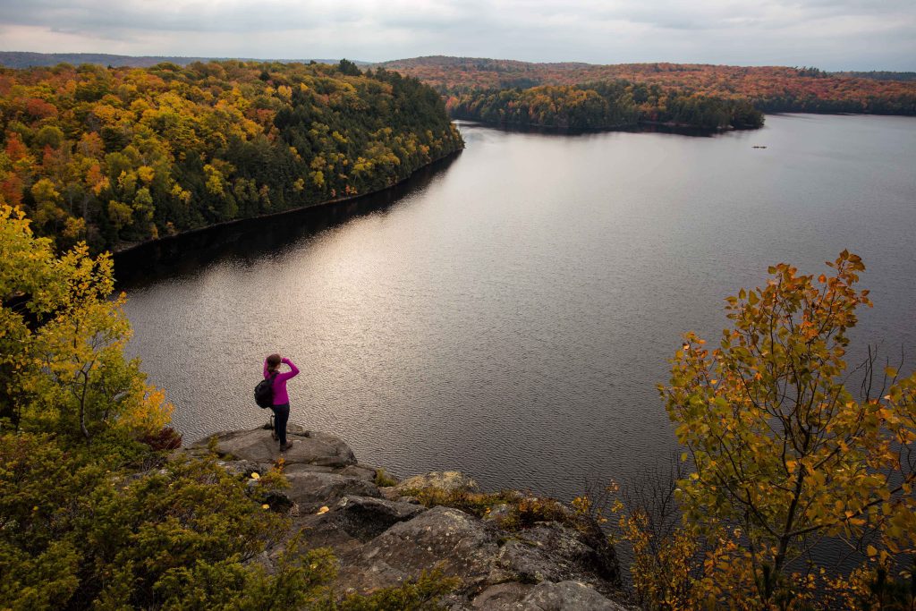hiker standing at lookout over lake circled with fall colours forest