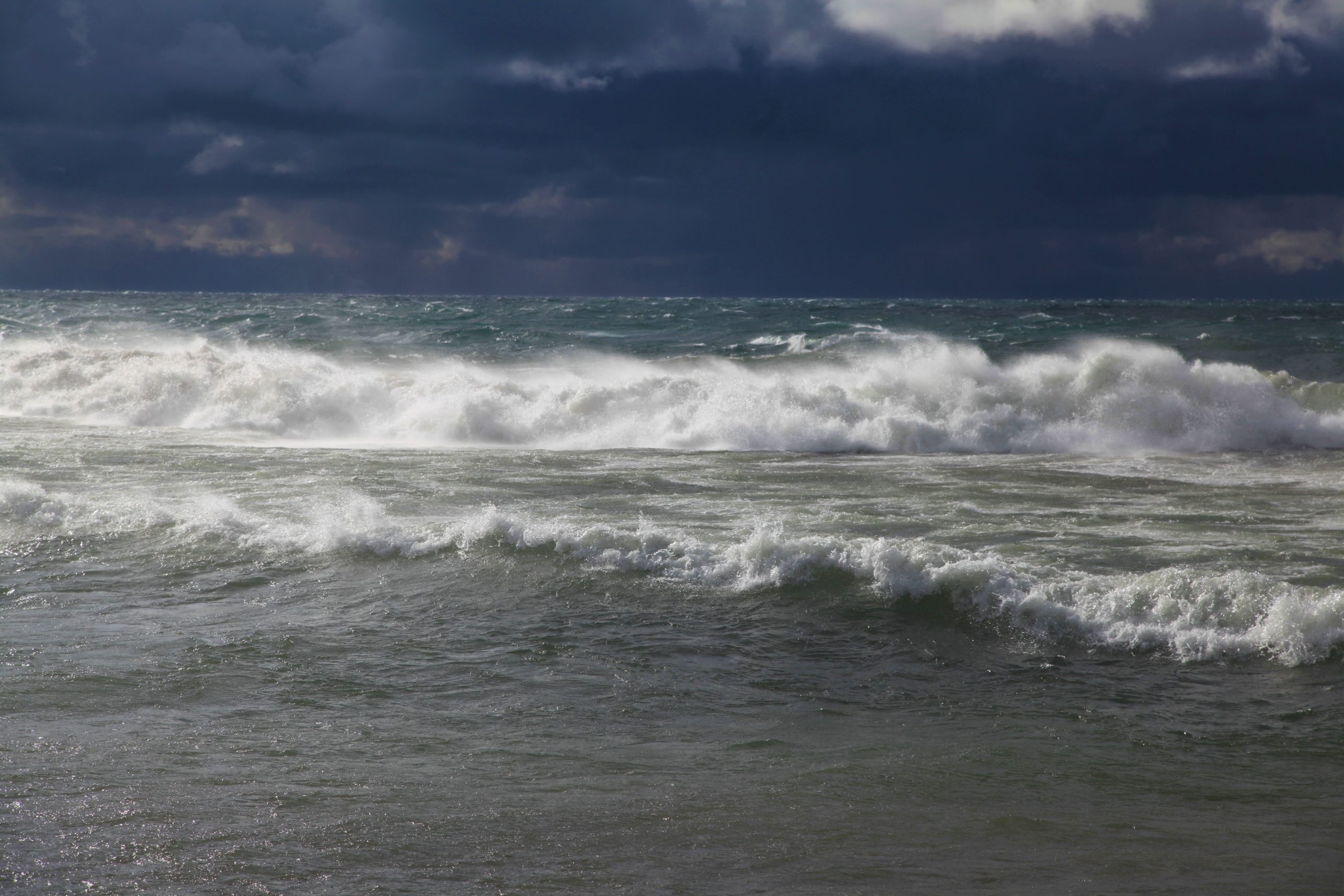 Large waves hitting the beach, with ominously dark clouds behind them on Lake Superior