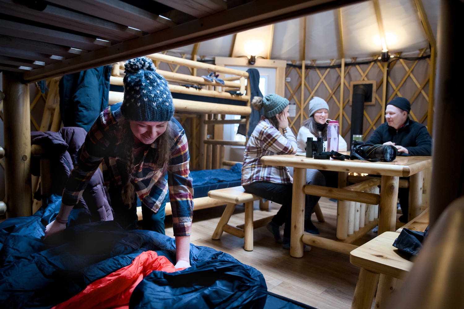 Four campers in yurt dressed in winter gear. Bunkbeds and wooden table.