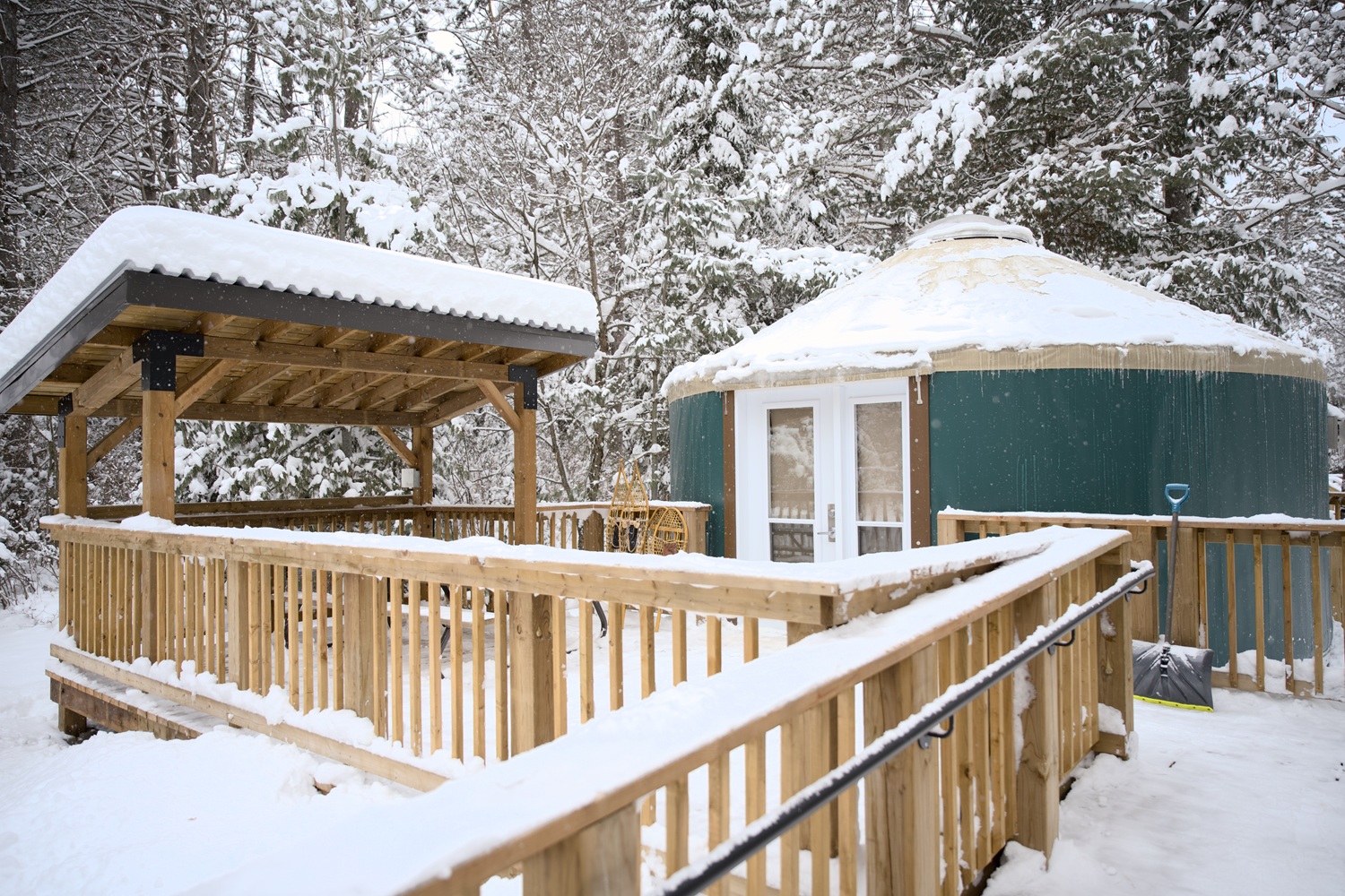 Green yurt and wooden porch with ramp, all covered in snow