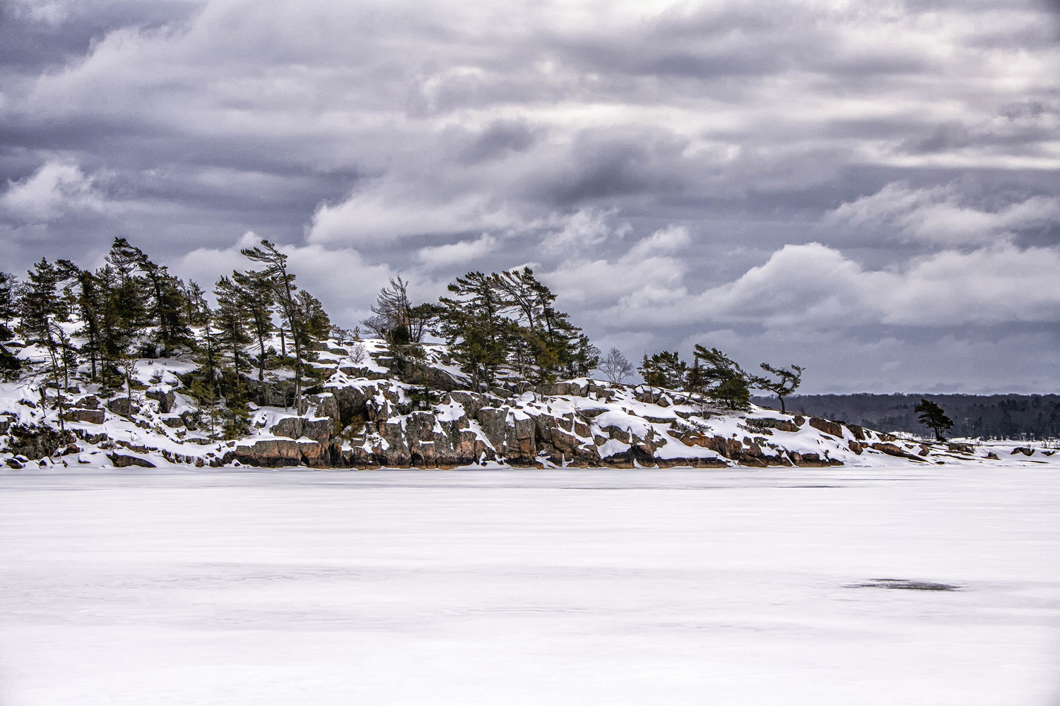 frozen snow-covered lake with rocky outcrop and evergreens