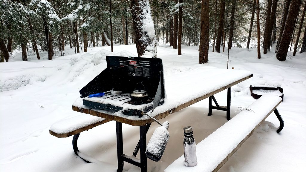 snow covered picnic table on campsite with stove