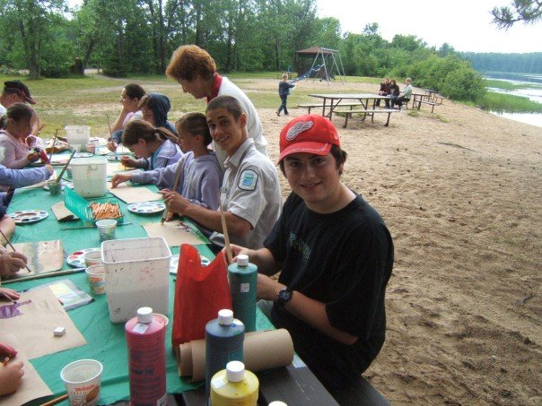 group sitting at picnic table on beach painting, staff sitting next to two children