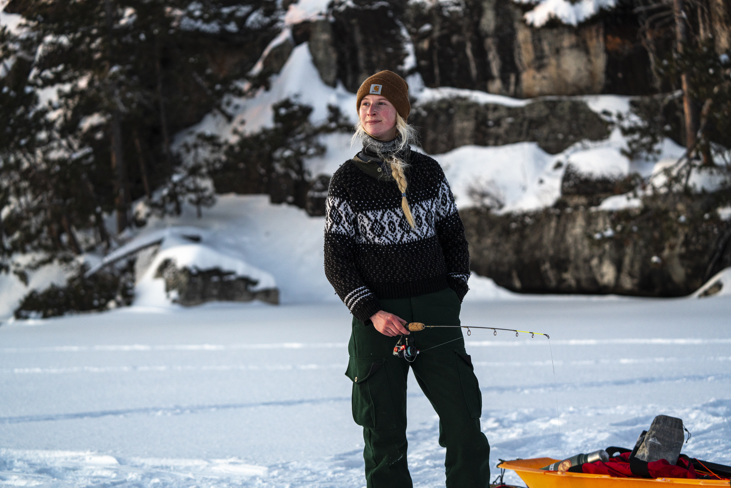 A person holding a fishing rod standing on a frozen, snow-covered lake