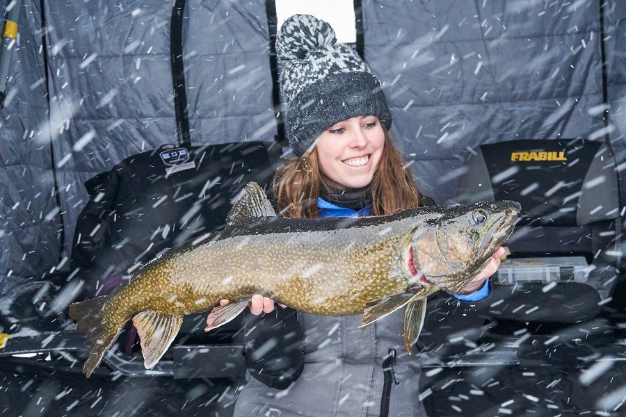 A smiling person holding a large fish outside as it snows