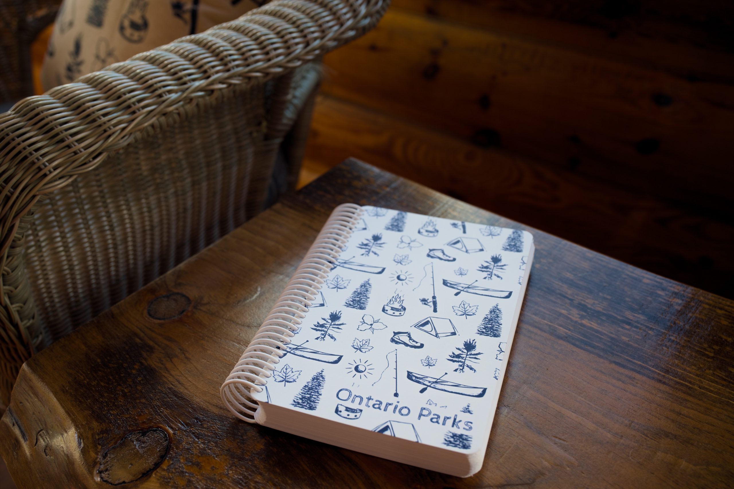 A spiral-bound notebook with blue camping-themed graphics on the cover resting on a wooden bench