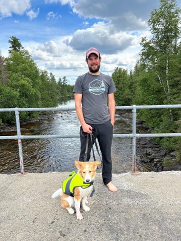 staff holding leash of dog wearing PFD, standing on bridge