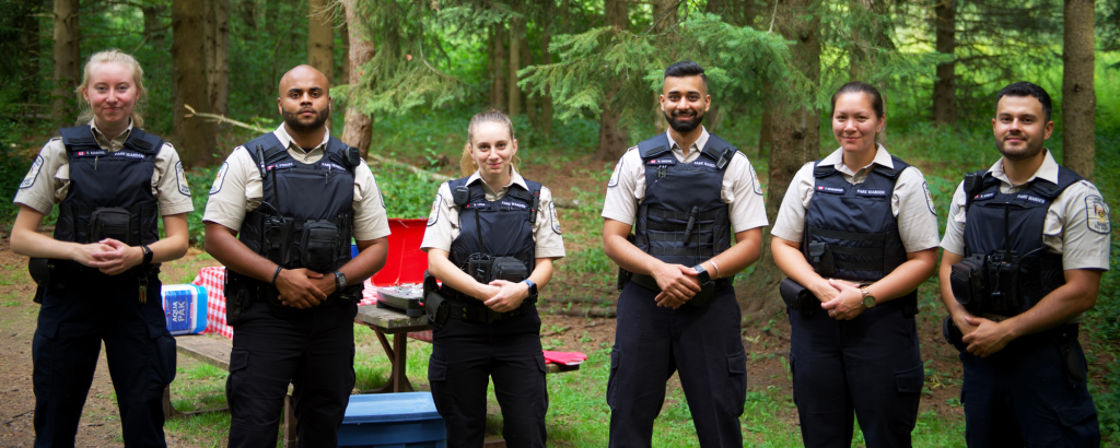 A group of park wardens standing in a line looking into the camera on a campsite