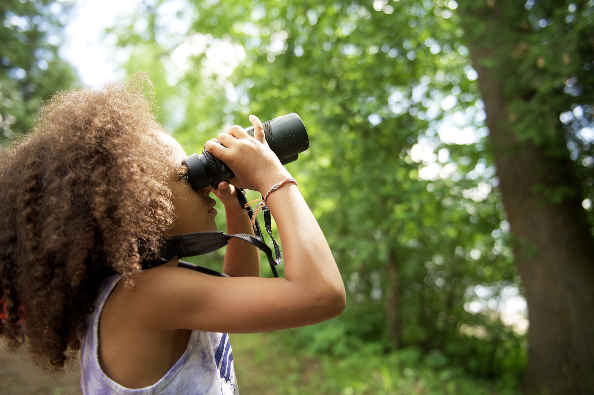 Child looking through binoculars in forest