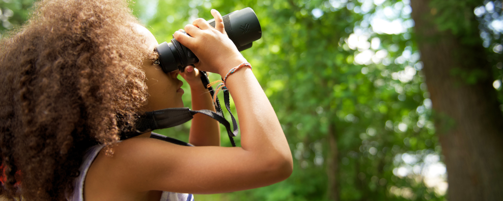 Child looking through binoculars in forest