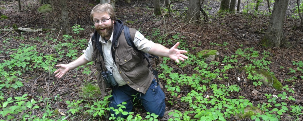Matt grinning while kneeling on the forest floor among green plants