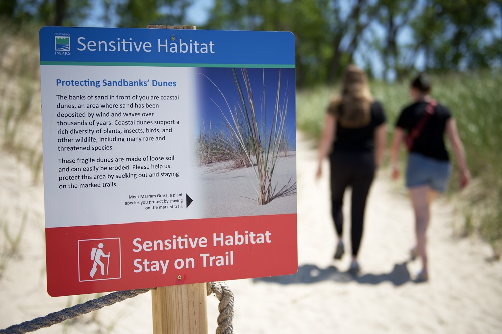 sensitive habitat trail sign with visitors walking in background