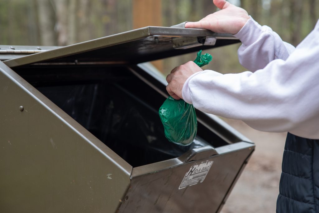 person throwing bag of dog poop in receptacle 