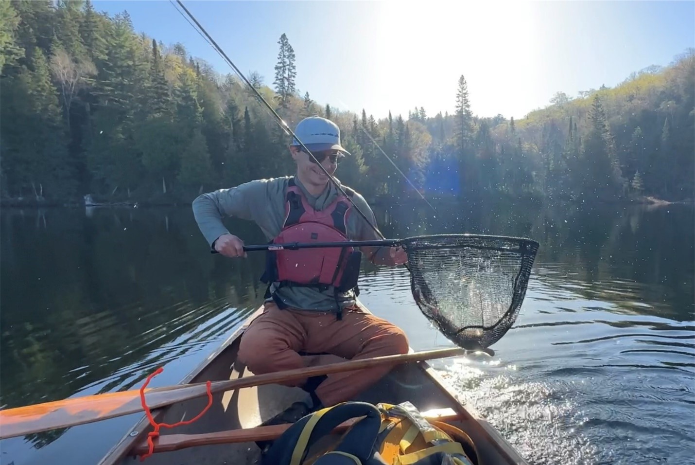 man seated in canoe on lake, holding fishing net