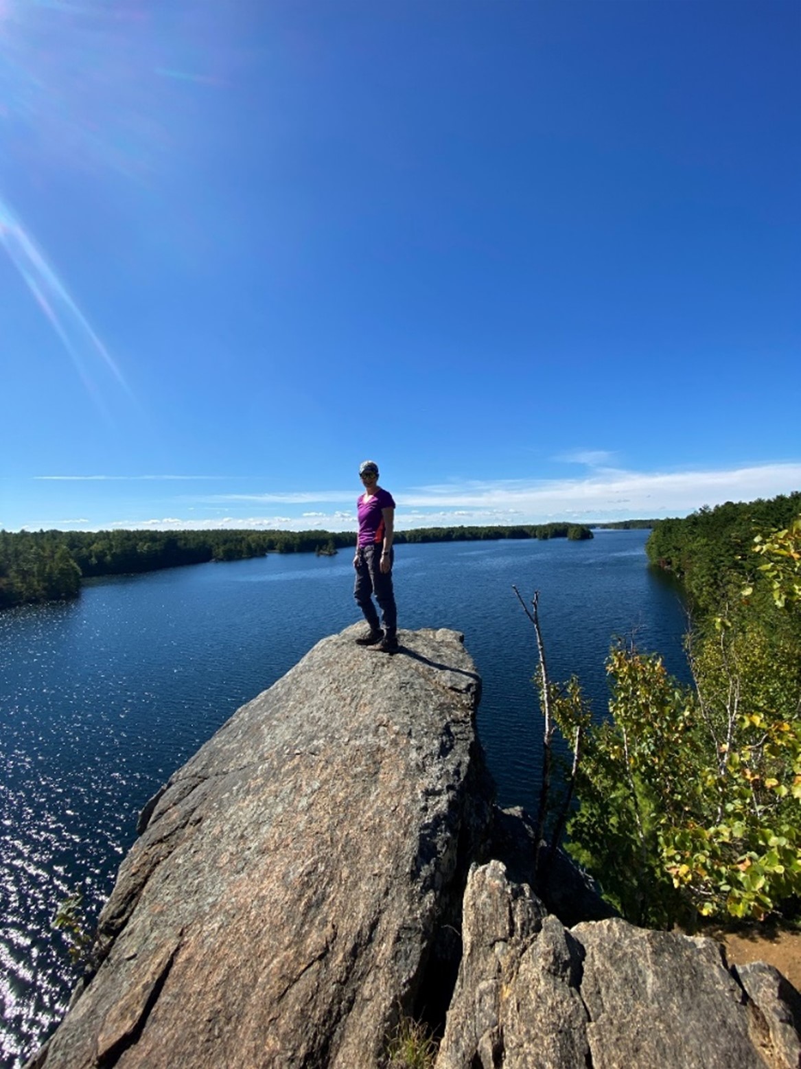 hiker standing on rock, looking out at glittering lake and forest