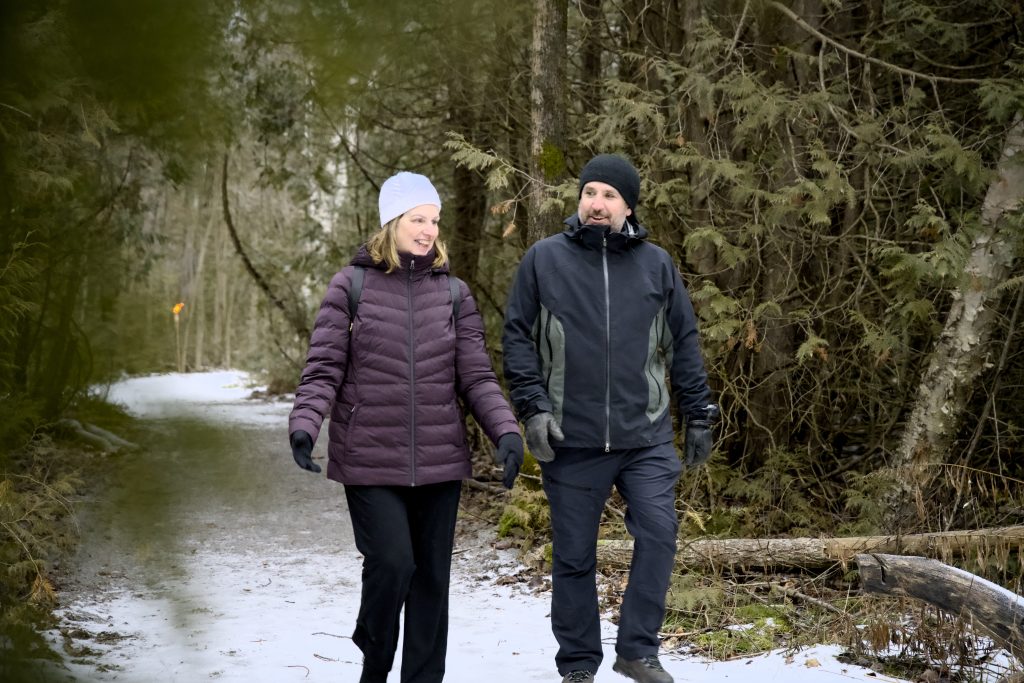 Two people walking on a lightly snowy path through the forest