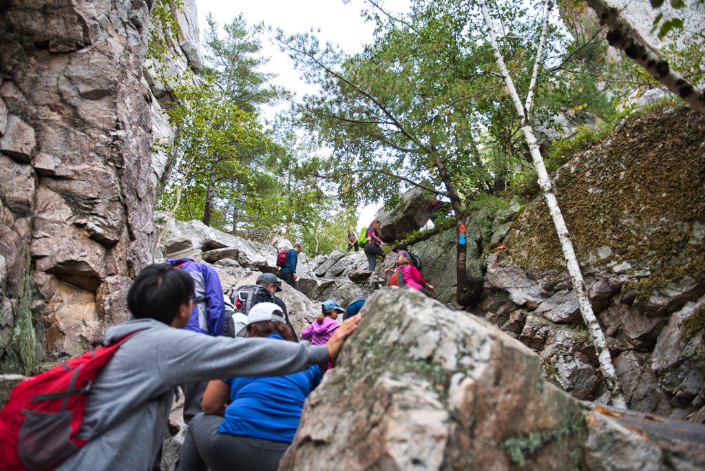 group of hikers climbing up rockface on trail