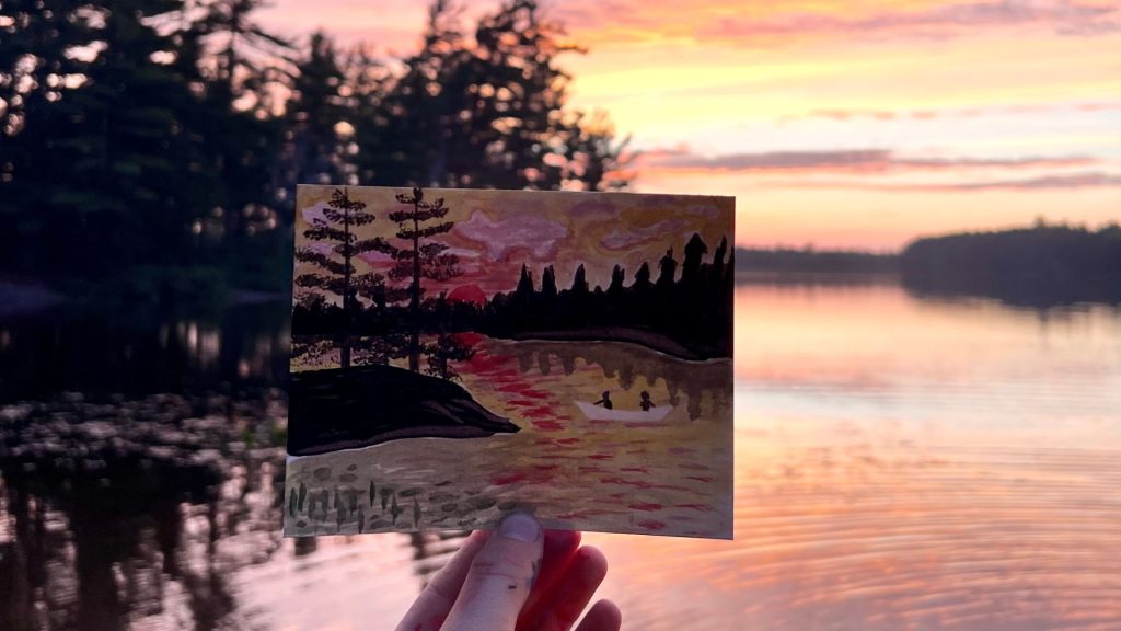 hand holding painting of sunset in front of sunset