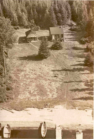 Photo aérienne aux tons sépia où l’on voit deux cabines dans un champ, entourées de forêt, et un rivage sablonneux à une extrémité