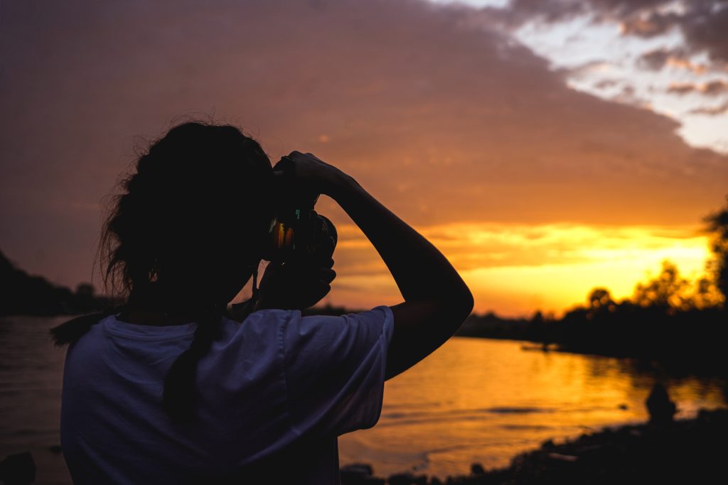 person taking photo of sunset over lake