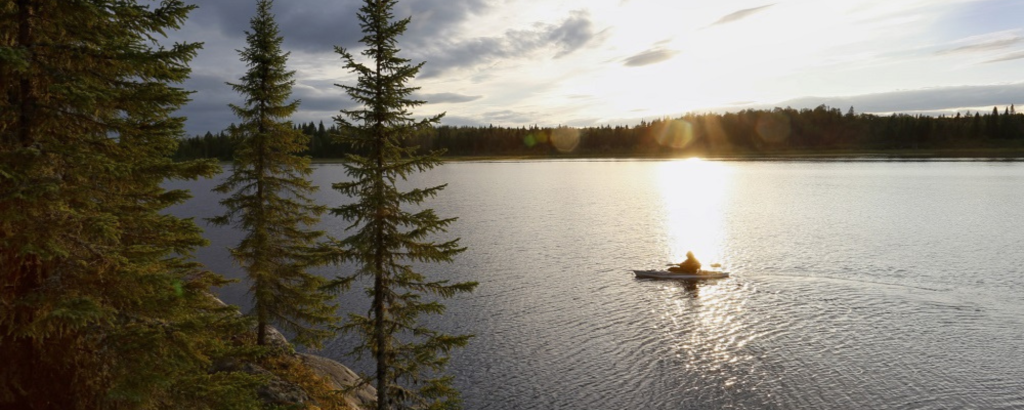 A kayaker on a lake with a forested and rocky shoreline