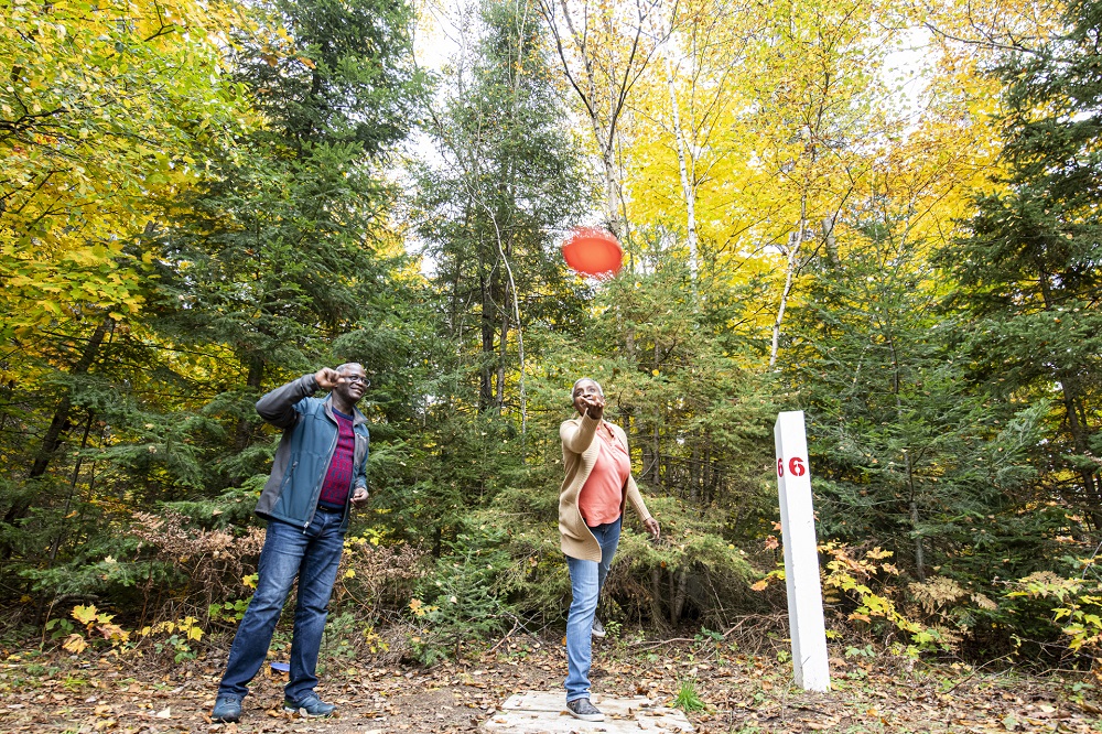 two people playing disc golf in forest with fall colours