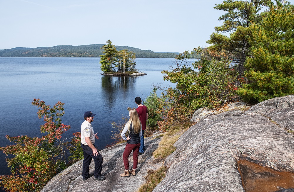 staff talking to two visitors at lookout over lake