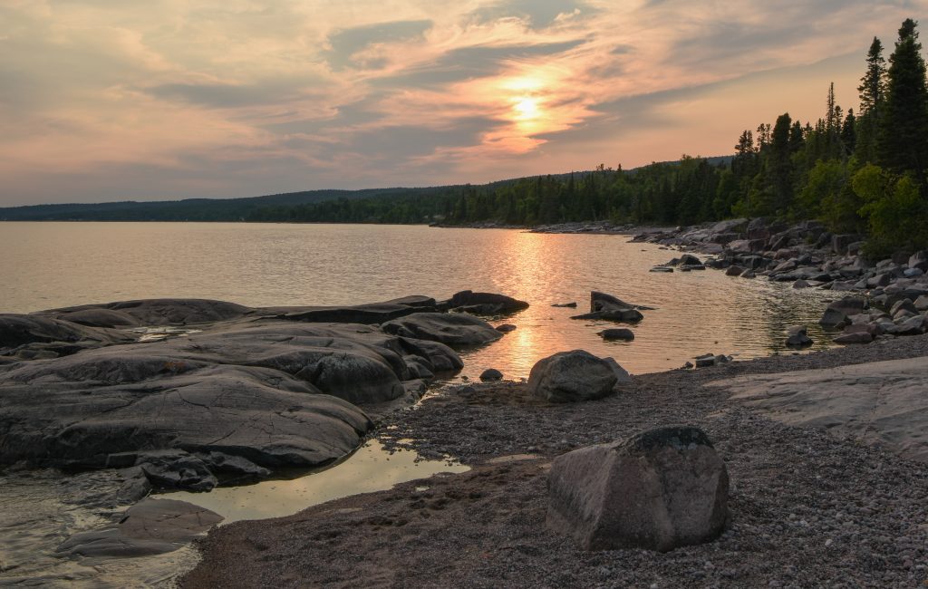 sun setting over rocky shore on lake