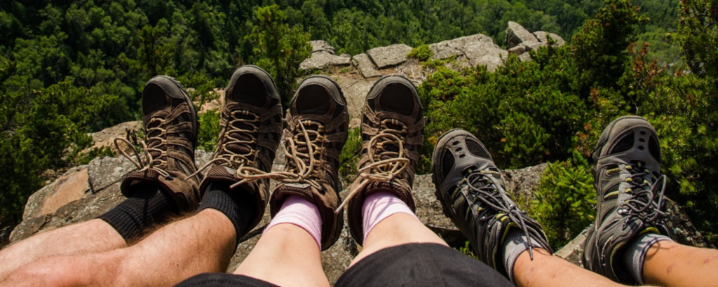Three people lower legs hanging off the cliff edge wearing hiking boots