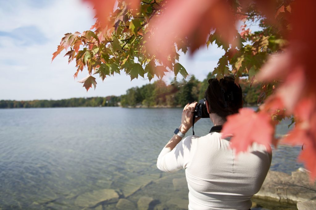 person taking photo of lake with fall colour foliage in foreground