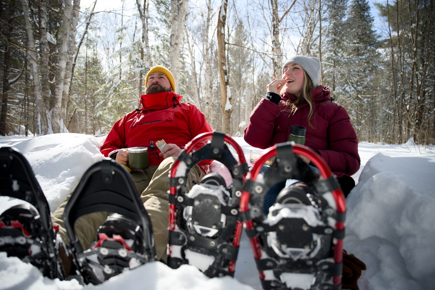 two snowshoers sitting down on the snowy trail for a snack
