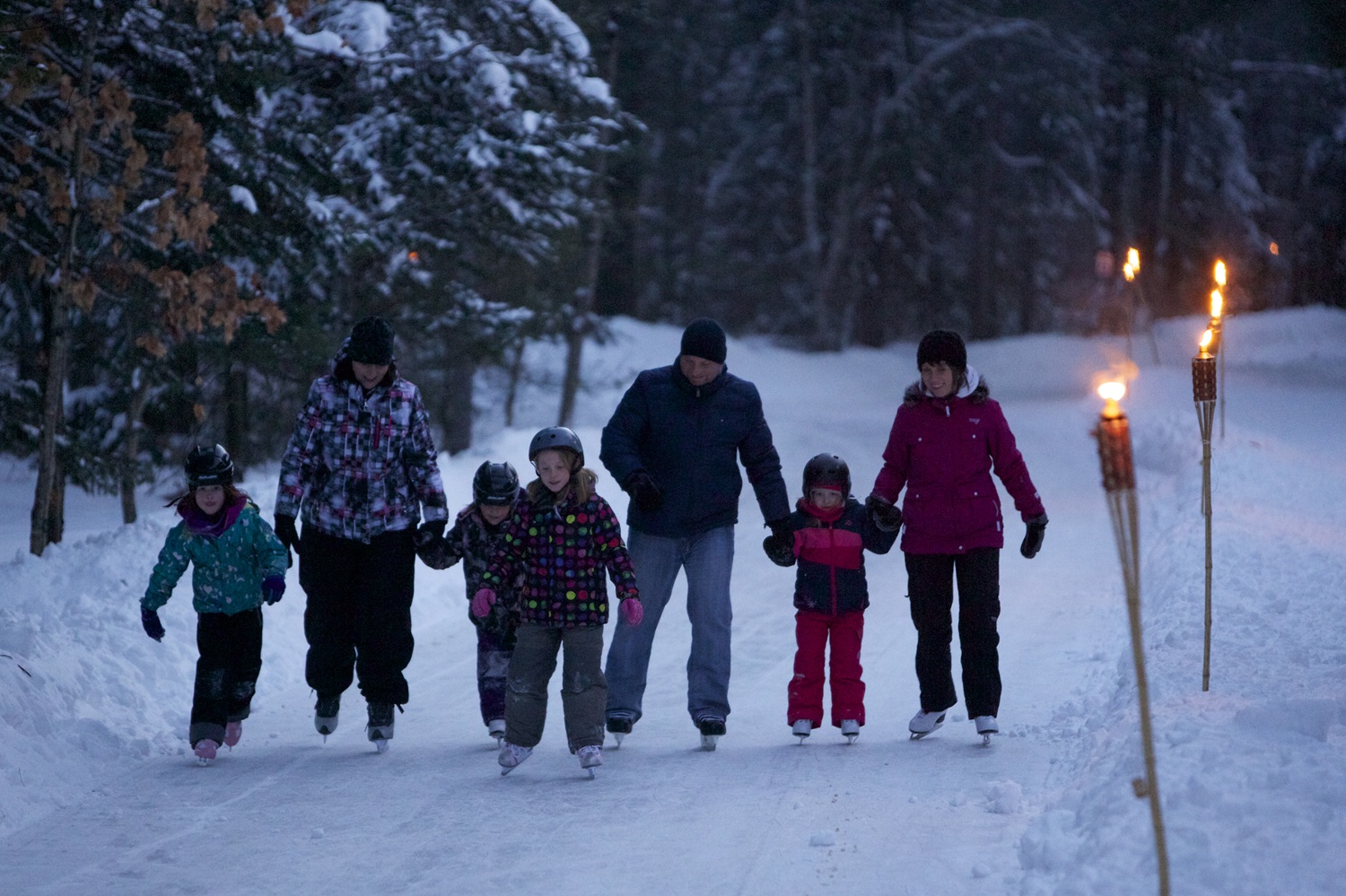 Families skating on the skating trail at night while the trail is lined with torches