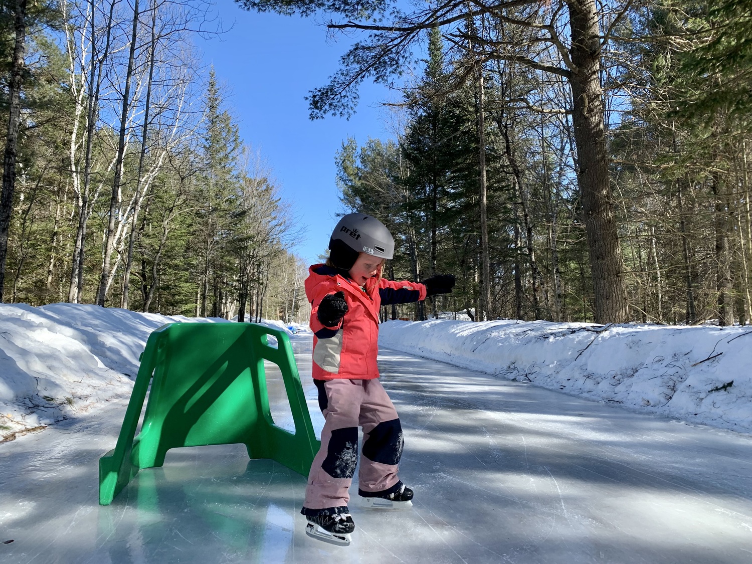 child skating on outdoor ice trail with green skate aid